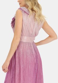 Sukienka bez rękawów o falbaniastym wykończeniu w gradientowych odcieniach różu, z plisowanym materiałem oraz paskiem w talii, wykonana z błyszczącego, refleksyjnego materiału.