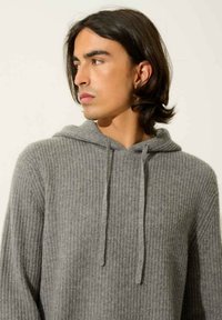 Szary, prążkowany hoodie z regulowanym ściągaczem, długimi rękawami i luźnym krojem, wykonany z miękkiego, teksturowanego materiału.