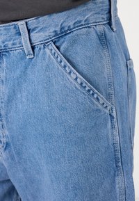 Lys blå denim bukser med høy midje, med en foran lomme, synlig søm og en teksturert stofffinish.