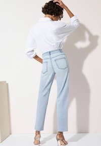 Jeans azzurri a vita alta con taglio dritto e due tasche posteriori, abbinati a una blouse bianca e sandali con tacco e tracolla.