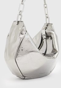 Sac à main en métal argenté avec une forme géométrique, surface texturée et une chaîne épaisse ; possède une fermeture éclair sur le côté.