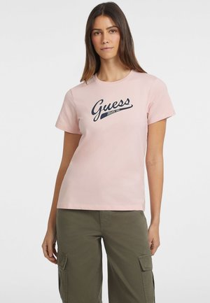 Jasnoróżowa koszulka z krótkim rękawem z granatowym logo "Guess Jeans 1981". Wykonana z bawełny, charakteryzuje się okrągłym dekoltem i luźnym krojem.
