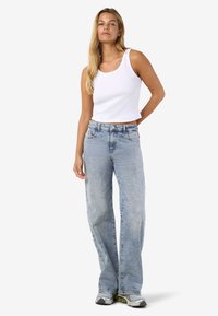 Svetlo modri visokorasli široki kavbojki z zbledelim videzom, v kombinaciji z belim rebrastim topom brez rokavov. Imajo zaponko na gumb in stranske žepe.