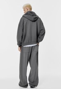 Sivá mikina s kapucňou a oversize strihom, spadnuté ramenné švy a textúrovaná látka, v kombinácii so širokými sivými nohavicami s bočnými vreckami.