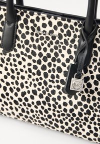 Sac fourre-tout imprimé léopard noir et blanc avec des poignées en cuir et un pendentif en argent avec le logo MK. Le matériau est texturé et doux.
