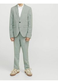 Jasnozielony garnitur z jedno guzikową marynarką, dopasowanymi spodniami i białą koszulą. Uzupełniony brązowymi i kremowymi sneakerami.
