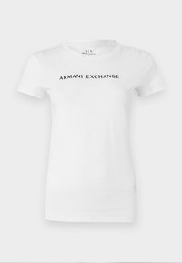 Bela majica iz bombaža s krojem na vratu. Na sprednji strani je črn napis "ARMANI EXCHANGE". Kratki rokavi, gladka tekstura.