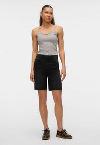 Pantalones cortos de mezclilla negros con corte recto y dobladillo deshilachado, combinados con una camiseta sin mangas de canalé gris. Zapatos marrones con cordones completan el conjunto.