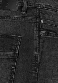 Black denim jeans featuring five pockets, contrasting stitching, a leather waistband label, and a smooth texture with a slight sheen.
