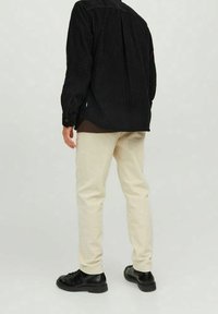 Camicetta in corda nera con taglio dritto, abbinata a pantaloni in corda color crema e scarpe nere stringate, vista da dietro.