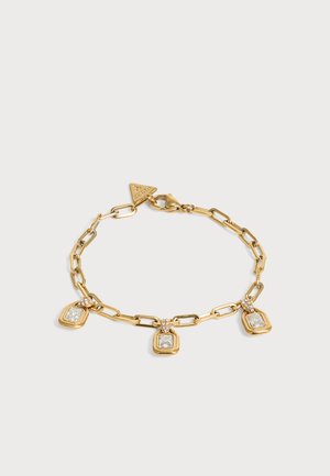 Bracelet chaîne en or avec trois breloques carrées en pierre précieuse transparente et une étiquette de marque triangulaire sur un fond clair.