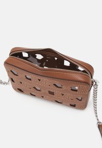 Brun læder crossbody taske med udskæringsmønster, sølv hardware, lynlås lukning og justerbar kædestrop. Glat og tekstureret finish.