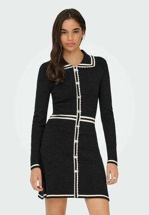 Must mustriibul olev must kudum, millel on valge laineline kaelus ja detailid, pikad varrukad ning nööpidega ees käiv kinnisosa dekoratiivsete nööpidega.