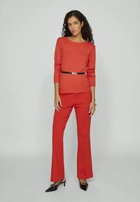 Sweater vermelho de malha com mangas longas e decote redondo, combinado com calças vermelhas largas. Um cinto preto realça a cintura.