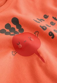 Pametna majica koraljne boje od pamuka s motivom crvene cikle koja ima nasmiješeno lice i ruke, uz igru riječi u crnoj boji. Glatka tekstura.