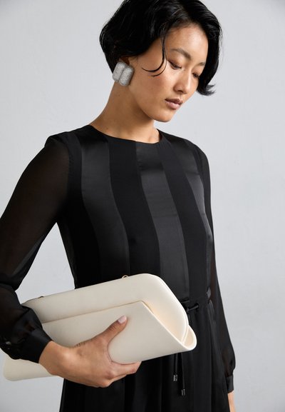 Robe noire à manches longues avec des rayures verticales en satin et un col rond, assortie à un sac à main crème à design plié.