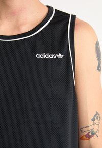 Mustmust vest, mis silikoonvõrgust, valgete äärtega kaeluses ja Adidas logo rinnal.