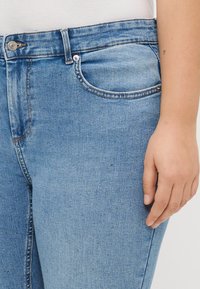 Blue denim jeans featuring a slim fit, subtle shiny embellishments, and a classic five-pocket design. Button closure and belt loops visible.