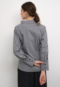 Striped blouse in black and white cotton, featuring a high collar and button cuffs. The back showcases a tailored fit and noticeable texture.