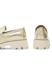 Pantofi slip-on metalici aurii cu o talpă albă voluminoasă. Prezintă o textură netedă, un design minimalistic și accente contrastante de nuanță bej la călcâie.