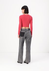 Sarkans ribots topiņš, apvienots ar pelēkiem platām biksēm, kurām ir melna kabata un redzamā šuvju apdare. Modelis redzams no aizmugures.