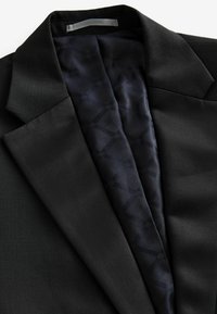 Schwarze Jacke aus glattem Stoff mit Satinrevers und einem strukturierten dunkelblauen Futter mit dezenten geometrischen Mustern.