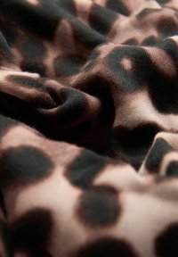 Leopardmönstrad tyg som visar en blandning av bruna och svarta nyanser med en mjuk, texturerad känsla. Har släta, flödande draperingar och djärva mönsterkontraster.