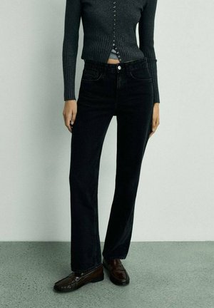 Black denim jeans with a straight-leg cut, featuring front pockets and a button closure. Paired with a dark ribbed sweater and brown shoes.