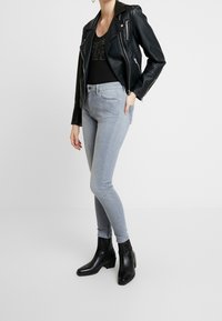 Černá kožená motorkářská bunda přes černý top, doplněná světle šedými úzkými džíny a černými kotníkovými botami na podpatku. Hladké textury a přiléhavý střih.