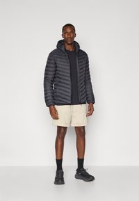 Puffer jacket in black with a quilted pattern, paired with beige shorts. Accessories include black socks and athletic shoes.