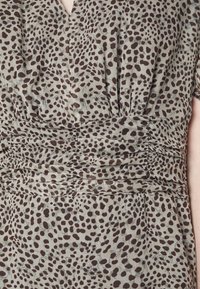 Acercamiento de un vestido color topo con manchas irregulares marrón oscuro y detalles de fruncido en la cintura y el busto.