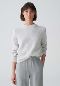 Hellgrauer, gerippter Strickpullover mit hohem Kragen und langen Ärmeln, kombiniert mit grauen, weiten Hosen mit Seitentaschen.