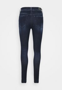 Vaqueros ajustados de color azul oscuro, hechos de denim, con bolsillos traseros y un parche de cuero de la marca en la cinturilla. Textura suave y forma entallada.