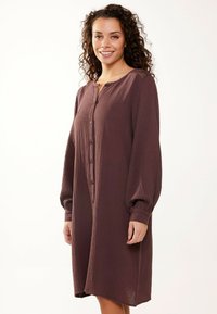 Abito button-up bordeaux realizzato in tessuto testurizzato, con maniche lunghe e vestibilità ampia, dotato di scollatura rotonda e tasche laterali.