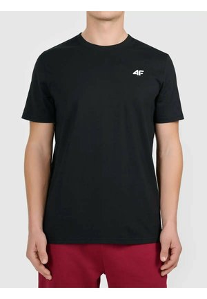 Mężczyzna noszący jednolity czarny T-shirt z krótkim rękawem i małym białym logo "4F" na klatce piersiowej, w połączeniu z ciemnoczerwonymi spodniami, na jasnym tle.