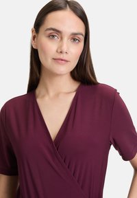 Bordeaux wikkeljurk met korte mouwen, gemaakt van zachte, gladde stof. Heeft een diepe V-hals en zachte draping voor een comfortabele pasvorm.