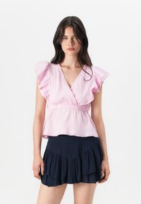 Haut rose clair à manches courtes avec des bords volants et un design enroulé, associé à une jupe superposée bleu marine, avec une texture plissée.