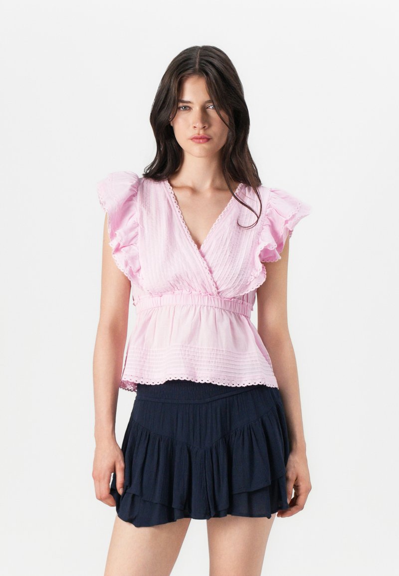 Haut rose clair à manches courtes avec des bords volants et un design enroulé, associé à une jupe superposée bleu marine, avec une texture plissée.
