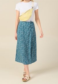 Vaaleankeltainen olkalaukku, valkoinen t-paita, kuviollinen turkoosi maksihame valkoisilla kukilla ja beiget platform-sandaalit hihnoilla.