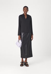 Blusa nera a maniche lunghe, design a V; gonna maxi in pelle nera con spacco laterale; tiene una borsa a tracolla viola chiaro; sandali neri con tacco.
