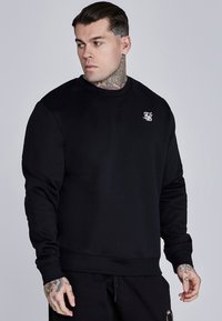 Sudadera negra hecha de una tela suave y elástica. Cuenta con un cuello redondo, mangas largas y un pequeño logo blanco en el pecho. Puños texturizados.
