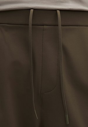 Olijfgroene broek met trekkoord in een gladde stof, voorzien van een voorzak en een platte tailleband, met bijpassende trekkoorden.