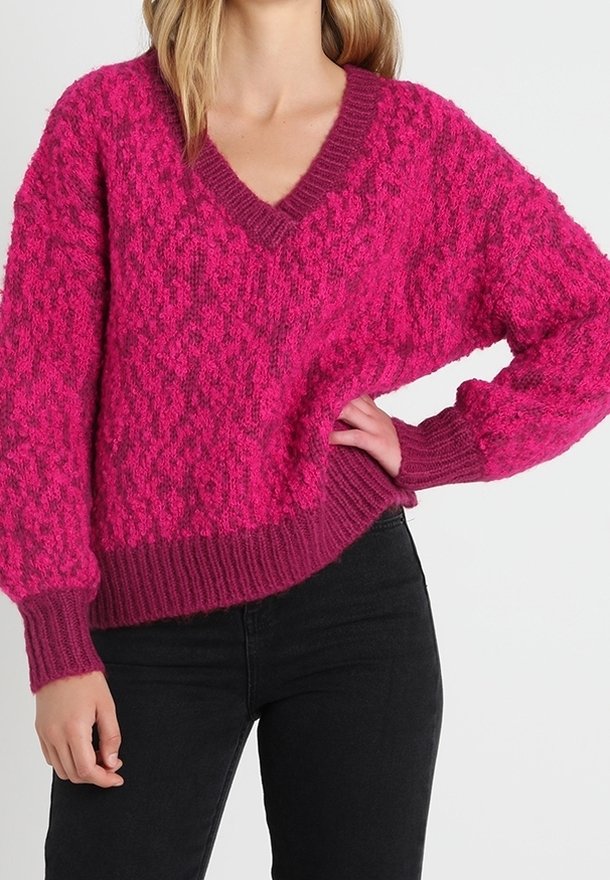 Rosa V-Ausschnitt-Pullover mit strukturiertem Strickmuster, gerippten Bündchen und Saum, kombiniert mit schwarzen Hosen. Der Pullover hat eine lockere Passform.