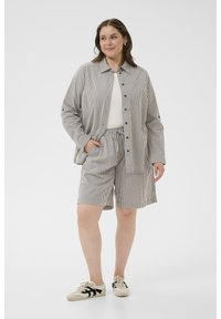 Tenue en tissu rayé comprenant une chemise boutonnée et un short à taille élastique dans des tons de beige et de bleu marine, associée à des baskets décontractées.