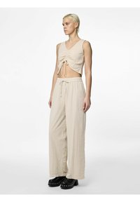 Beige kortärmad blus med samlad framtill och knytband, tillsammans med lösa, högmidjade beige byxor, bärs med svarta plattformsskor.