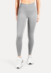 Leggings gris clair en tissu extensible, dotés d'une taille haute et d'une texture lisse, associés à des chaussures de sport blanches.