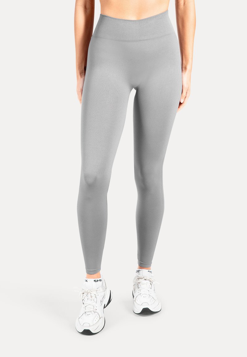 Leggings gris clair en tissu extensible, dotés d'une taille haute et d'une texture lisse, associés à des chaussures de sport blanches.
