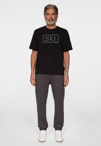 Mustat t-paidat harmaalla "SKI" logolla, yhdistetty harmaisiin college-housuihin ja valkoisiin tennareihin. Klassinen malli ja pehmeä materiaali. Yksinkertainen muotoilu, ilman kuvioita.