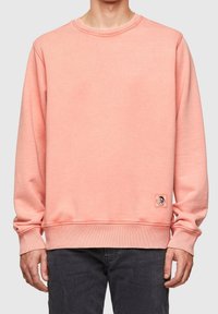 Light pink sweatshirt with a round neckline, ribbed cuffs and hem, and a small logo patch on the lower left side. Soft textured fabric.