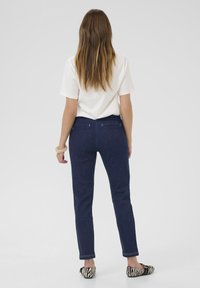 Jeans en denim bleu foncé avec une coupe slim, dotés de poches arrière et de coutures blanches, associés à des ballerines rayées noir et blanc.